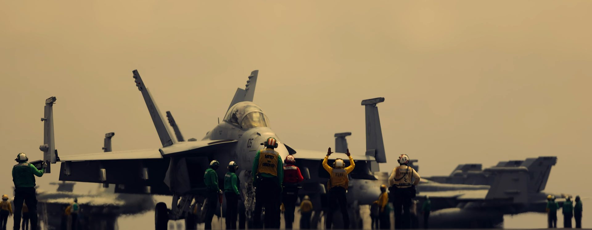Flight deck crew directing a Hornet on the carrier at golden hour