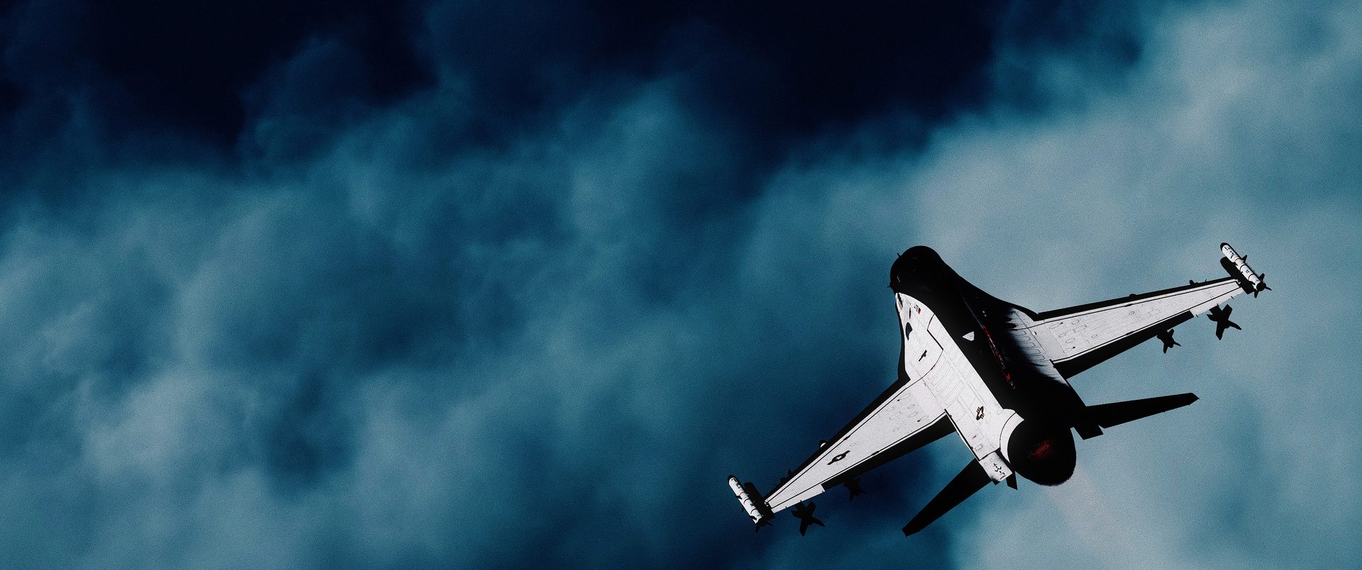 An F-16C seen from below against dark clouds
